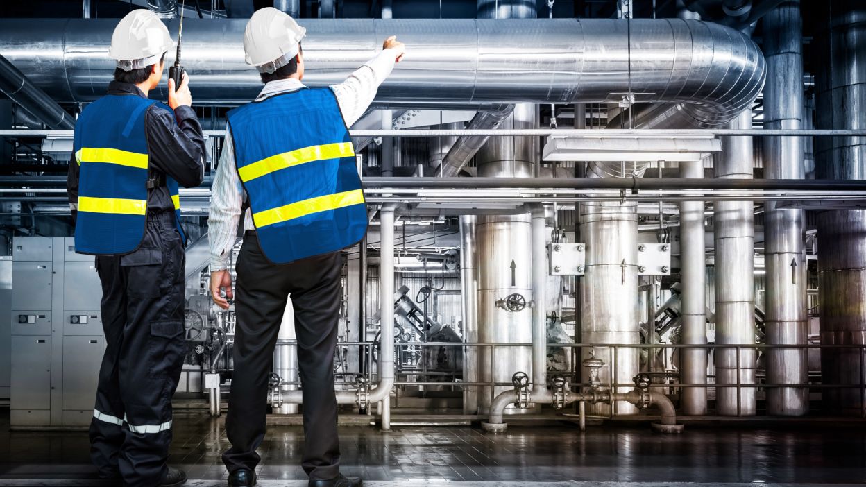 dos trabajadores delante de una tubería industrial en una planta química